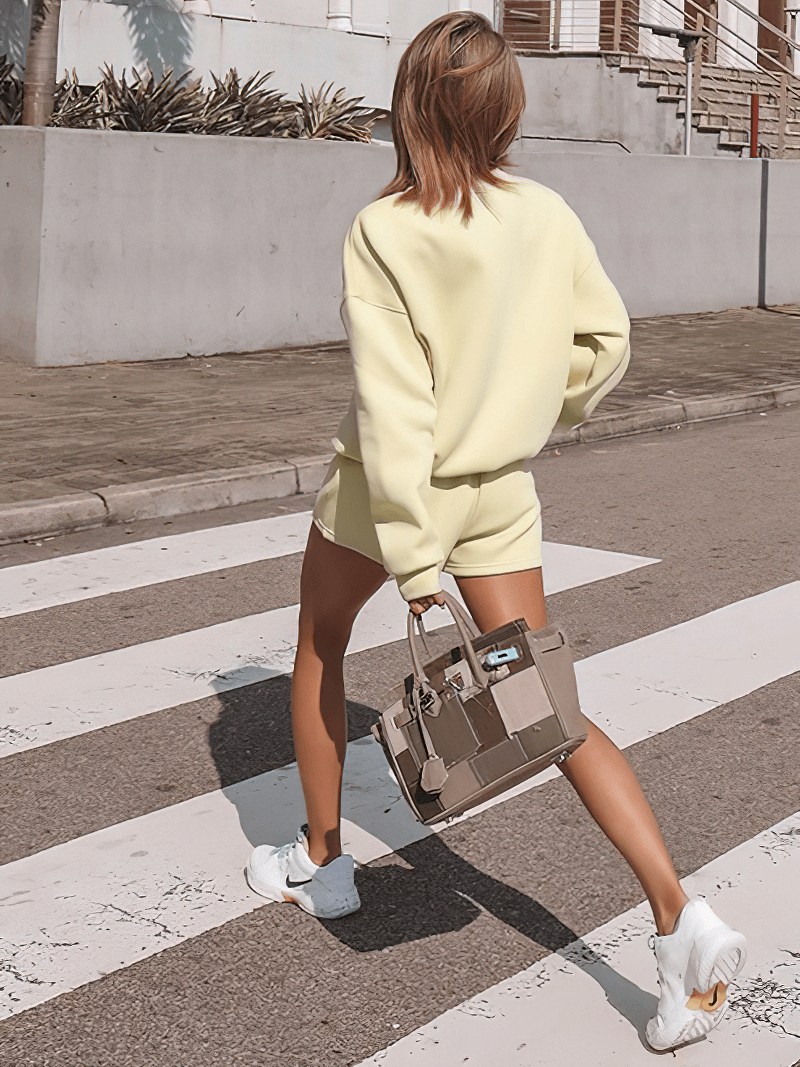 Woman in letter embroidery solid color sweatshirt and shorts crossing street, casual chic style, with handbag and sneakers.